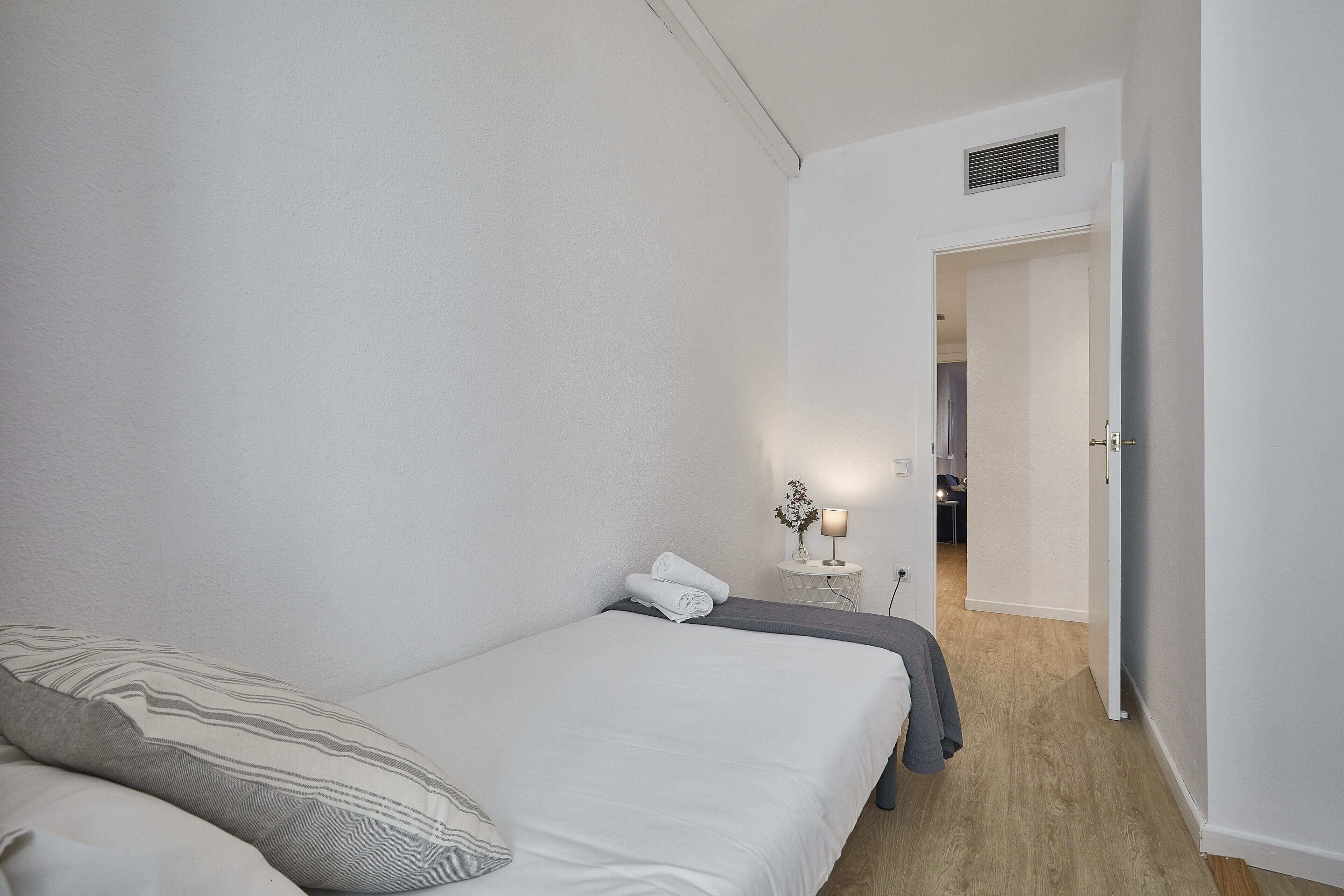A bedroom with a bed, pillows, a bedside table with a lamp, and a door leading to another room.