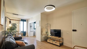 Ein modernes Wohnzimmer mit einer Couch, einem Fernseher auf einem Lowboard, einem Essbereich und einer Küche im Hintergrund.