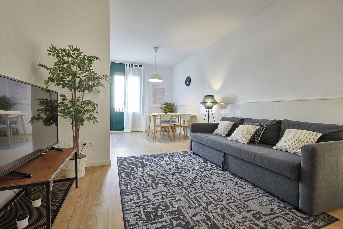 Ett modernt vardagsrum med en grå soffa, ett mönstrat matt och en tv som står på ett träställ.