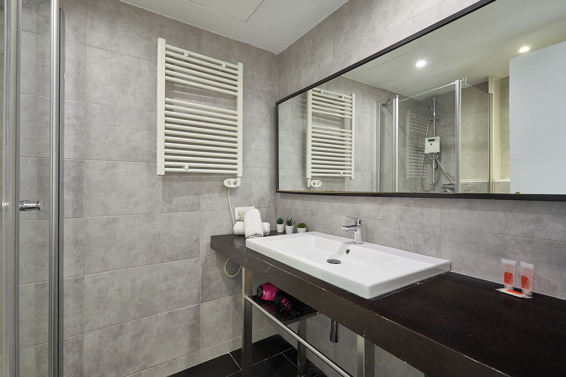 A modern bathroom with a large mirror, a white sink, and a shower area.