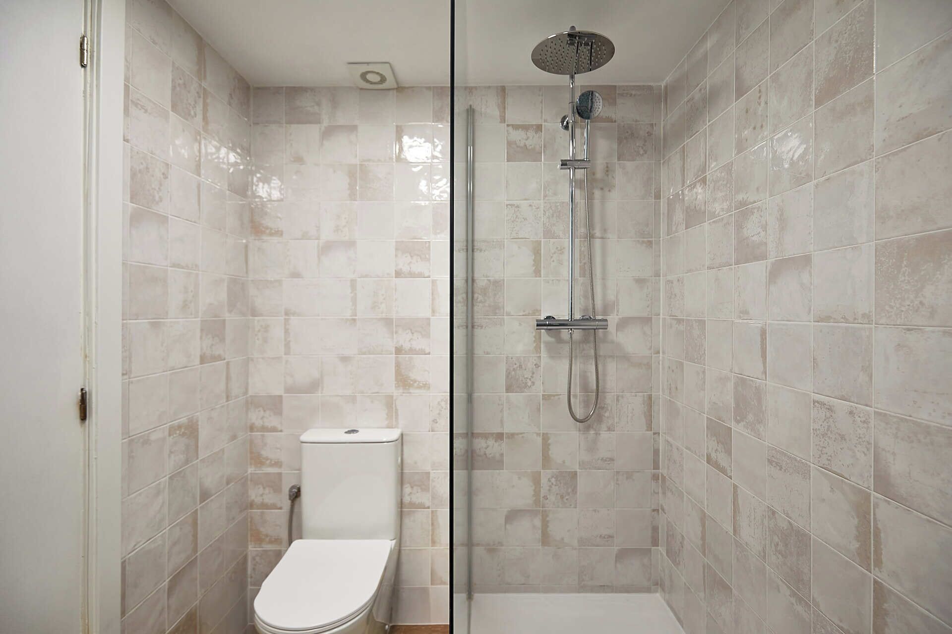 A bathroom with a glass-enclosed shower, a toilet, and tiled walls.
