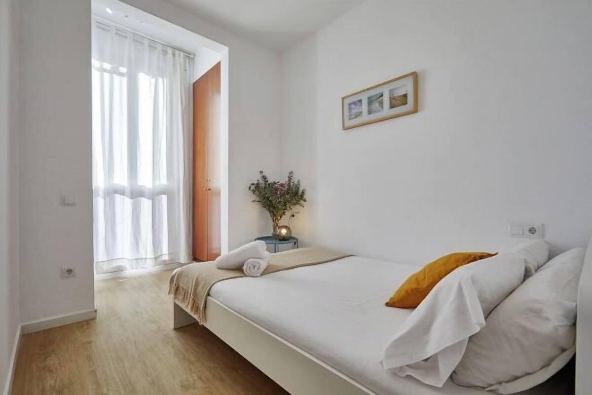 A bedroom with a bed, a nightstand, a window with curtains, and a wall-mounted picture.