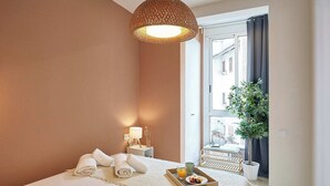 Ein Hotelzimmer mit Bett, Nachttisch mit Lampe, Tablett mit Frühstücksangeboten und Blick nach draußen.