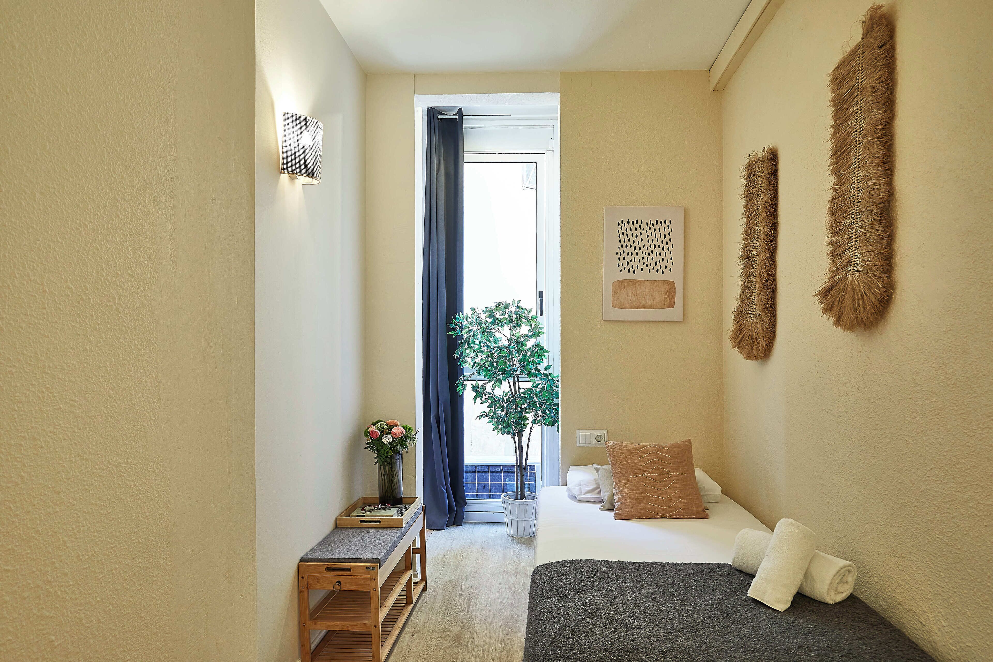 Een kleine, knusse kamer met een bed, nachtkastje, een potplant en een wandlamp.