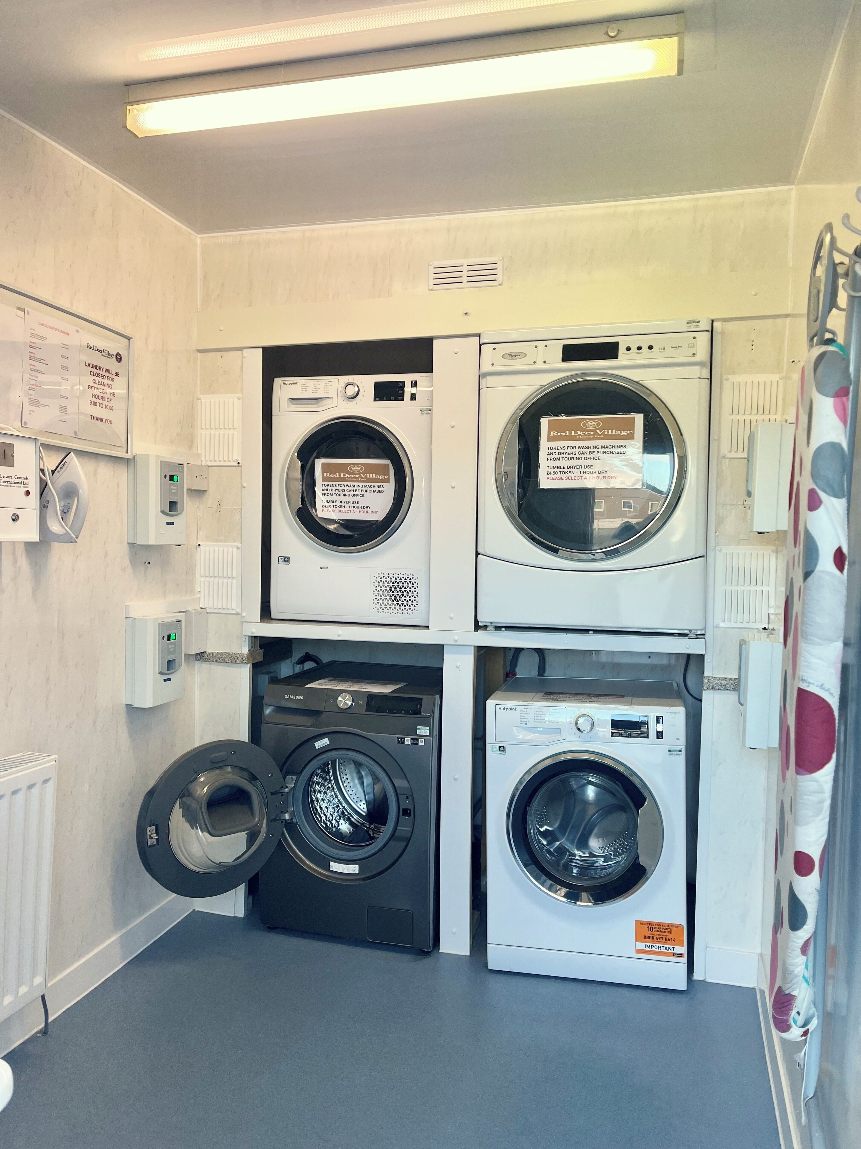 A laundry facility with multiple washing machines and dryers, control panels, and a sign indicating the cost of using the machines.
