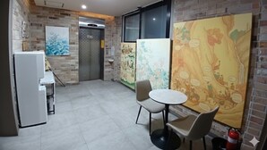 A room with a brick wall, a white refrigerator, a small table with chairs, and a large colorful mural. - Paradise Hotel (Icheon)