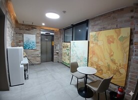 Una habitación con pared de ladrillo, un refrigerador blanco, una pequeña mesa con sillas y un mural grande y colorido.