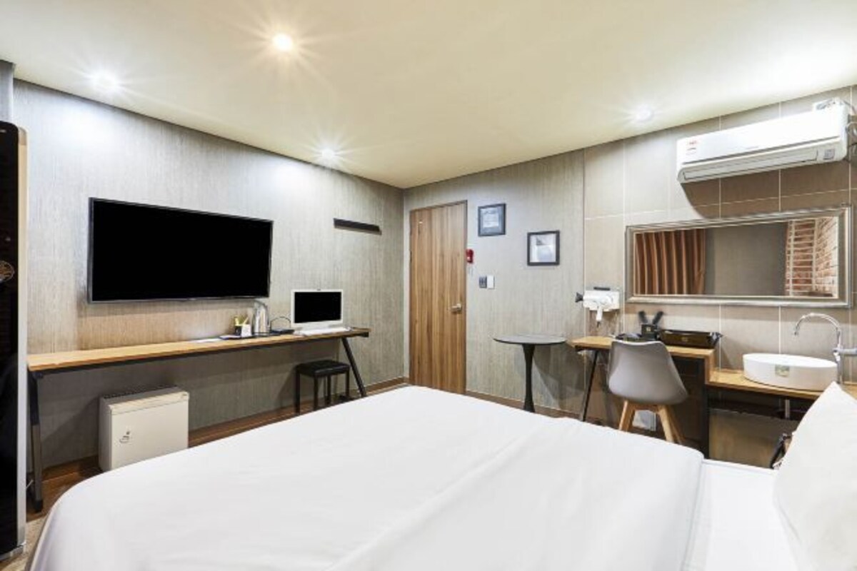 A hotel room with a bed, desk, chair, television, and a small kitchenette.