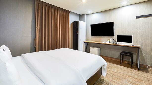 Ein Hotelzimmer mit einem Bett, einem Schreibtisch mit Computer, einem Fernseher und einem Kühlschrank.