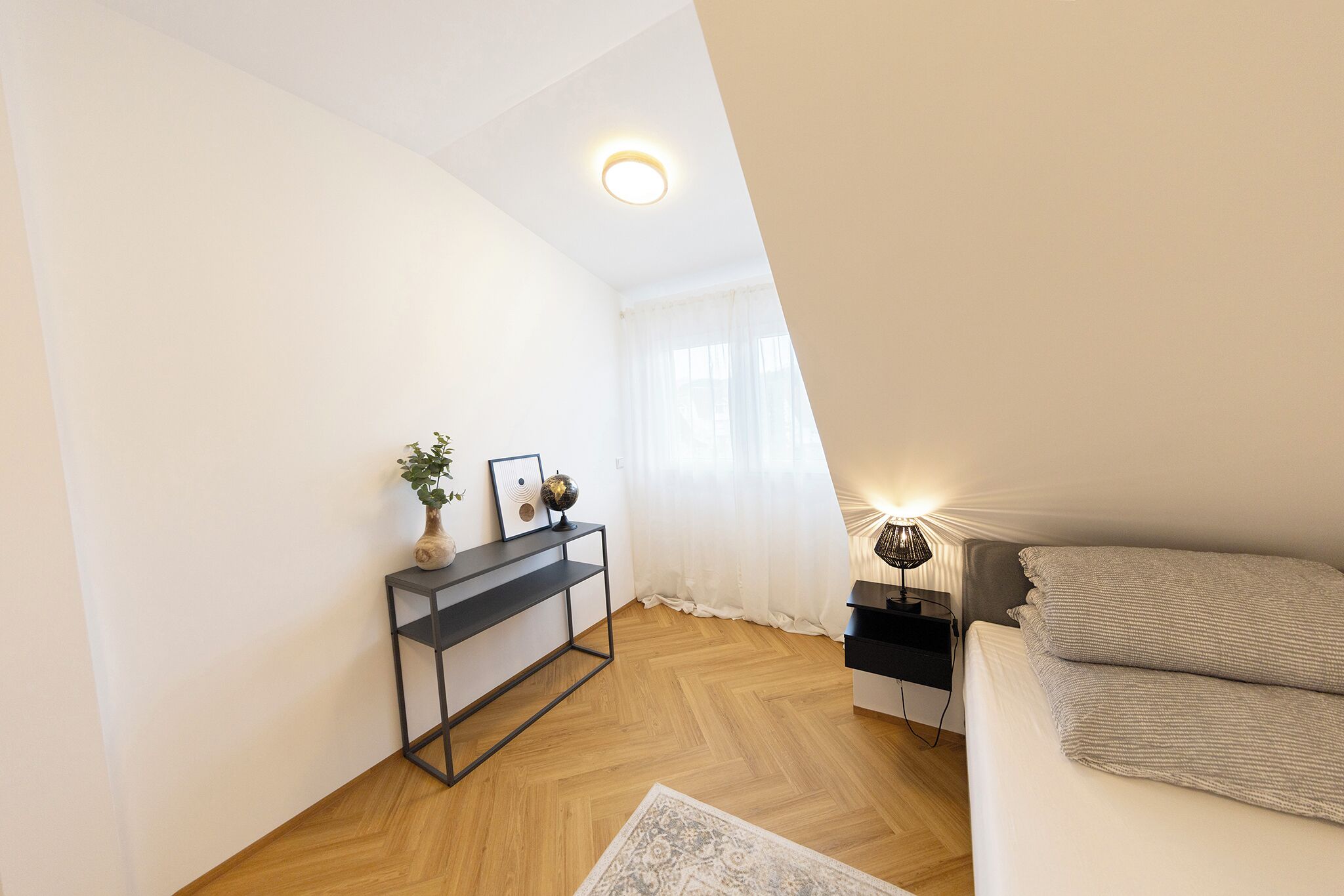 Ein Schlafzimmer mit Bett, Nachttisch, Lampe und einer kleinen Konsole mit Dekoration.