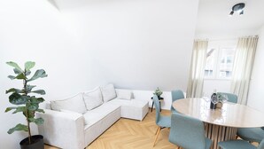 A modern living room with a sectional sofa, a dining table with chairs, a potted plant, and a window with curtains. - Exclusive apartment “Tony”
Modern living for up to 6 people in a prime location (Küssaberg)