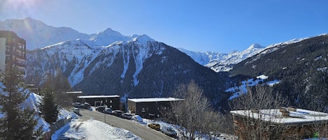 A snowy mountain landscape with a road, buildings, and parked cars.