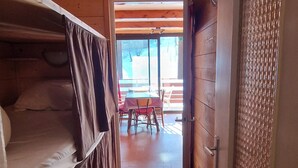 A wooden interior with a bunk bed, a dining table with chairs, and a view of the outside. - Renovated T2 apartment at the slopes, for 6 guests (Enchastrayes)