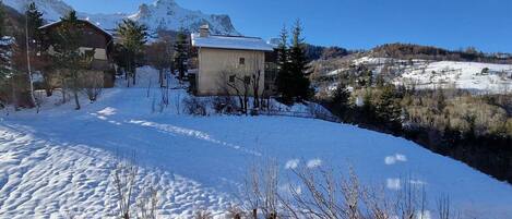 Een besneeuwd landschap met een huis en bergen op de achtergrond.