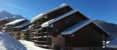 Une rangée de bâtiments en bois dotés de balcons, se dressant sur fond de montagnes enneigées.