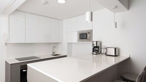 Une cuisine moderne avec des meubles blancs, un îlot central, un four à micro-ondes, une machine à café et un grille-pain.