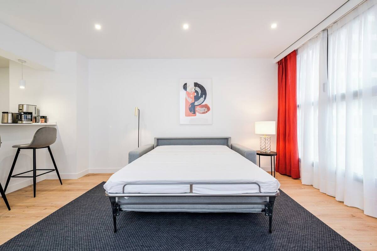 A modern bedroom with a bed, a desk, a chair, and a red curtain.