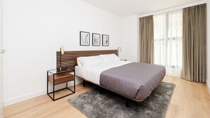 Une chambre à coucher avec un lit, une table de chevet, une fenêtre avec des rideaux et trois tableaux encadrés accrochés au mur.