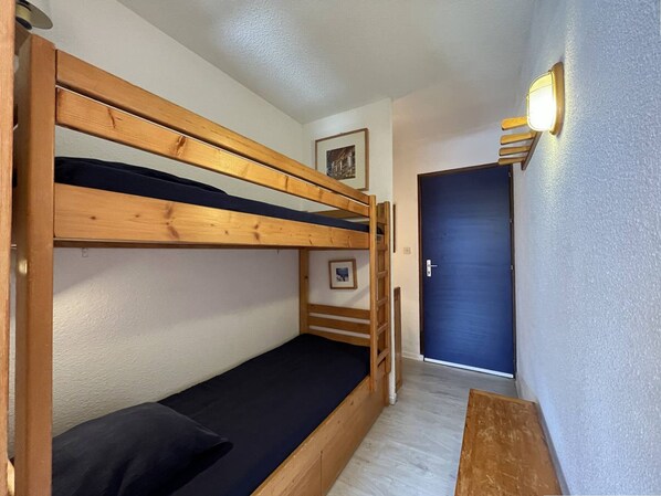 A bunk bed room with a wooden ladder, a blue door, and a small picture on the wall.