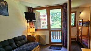 A compact room with a sofa, a television, a bunk bed, and a window with a view of a building and greenery. - Studio for 4 near slopes, balcony, pets allowed - Vallandry (Peisey-Vallandry)