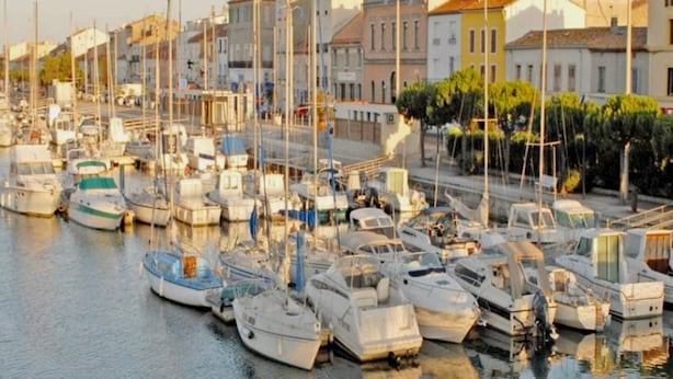 Puerto deportivo con barcos amarrados, rodeado de edificios de arquitectura diversa.