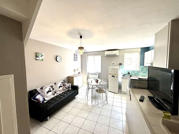 A compact living space with a sofa, dining table, chairs, a TV, and a kitchenette.