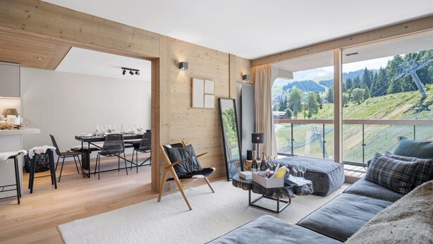 Una sala de estar moderna con un ventanal que ofrece vistas a la montaña, una zona de comedor con mesa y sillas de madera, y un rincón de descanso acogedor con un sofá y una mesita de centro.