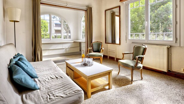 Una habitación acogedora con una cama, una mesa, dos sillas y ventanas grandes.