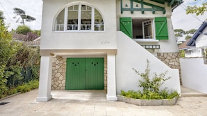 Una casa de dos pisos con una puerta verde, un balcón y un muro de piedra.