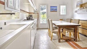 Una cocina moderna con armarios blancos, un ventanal grande y un comedor con mesa y sillas de madera.