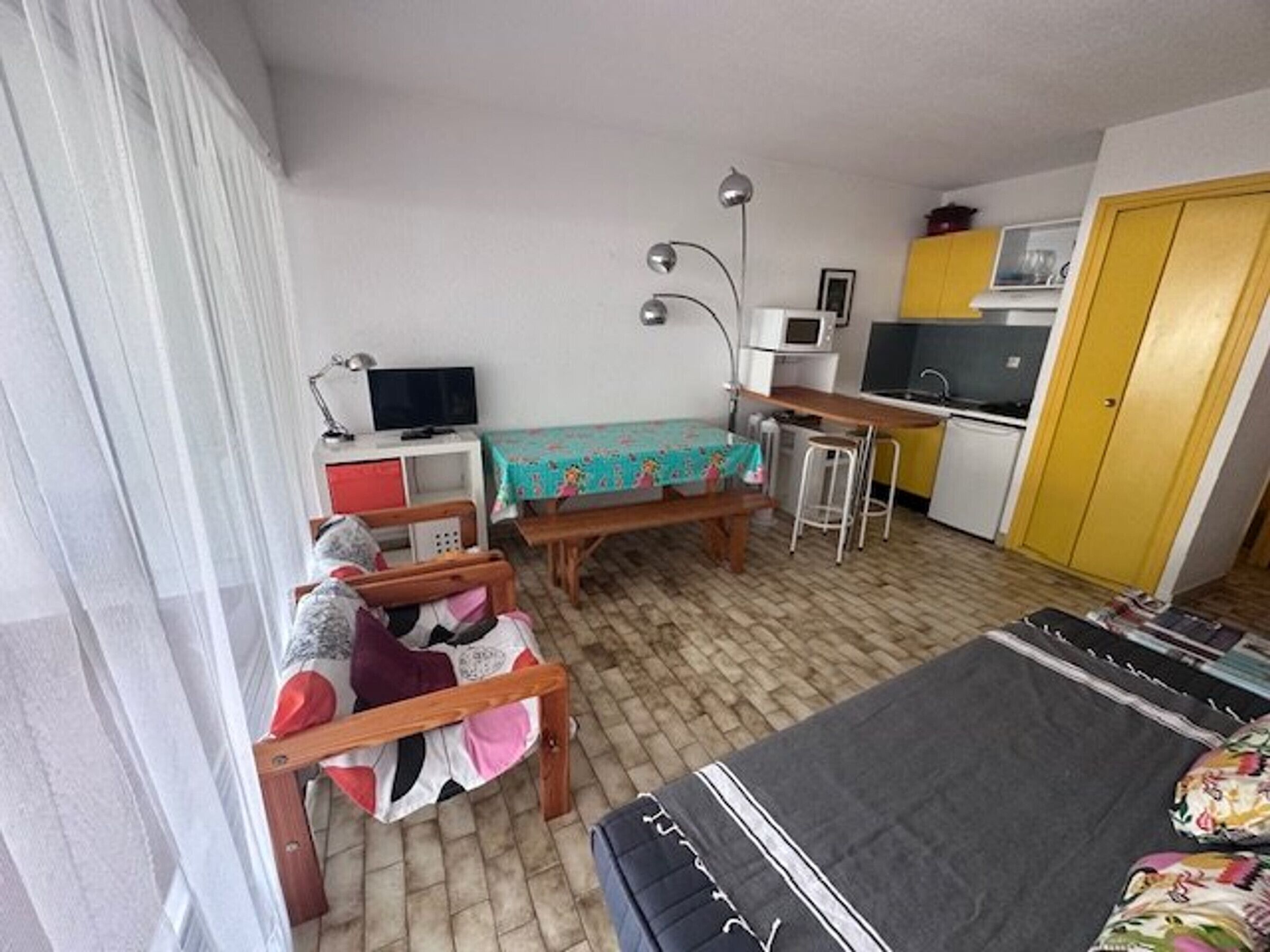 A compact room with a bed, a desk, a chair, a small kitchenette, and a window with curtains.