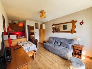 A cozy living room with a wooden dining table, a grey sofa, and a red lamp.
