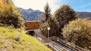 Une cabane en bois dotée d’un balcon, entourée d’une végétation luxuriante et avec des montagnes en toile de fond.