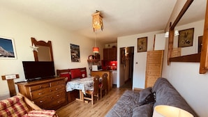 Un salon chaleureux avec un canapé, une commode en bois, un téléviseur et un coin repas comprenant une table et des chaises.