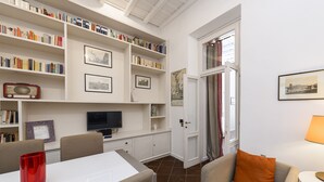Una habitación con una mesa de comedor, sillas, una estantería, un televisor y una puerta que da a otra habitación.