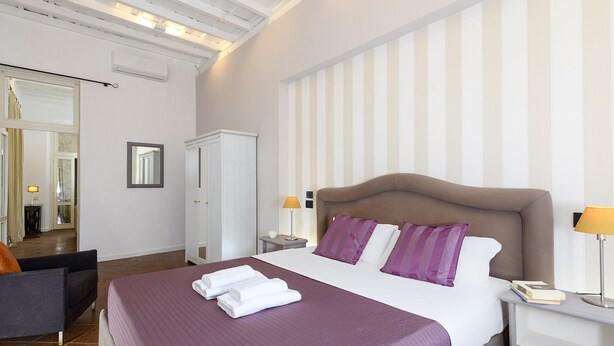 Una habitación de hotel con una cama grande, una mesita de noche, una silla y un armario.