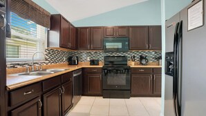A kitchen with dark wooden cabinets, a black stove, and a stainless steel refrigerator.