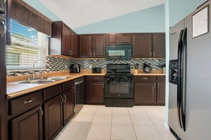 A kitchen with dark wooden cabinets, a black stove, and a stainless steel refrigerator.