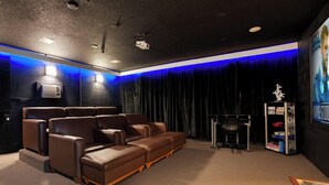 A home theater room with a sectional sofa, a ceiling-mounted projector, and a wall-mounted screen.
