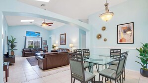 A spacious living area with a glass dining table, leather sofas, and a ceiling fan.