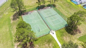 Vista aérea de una cancha de tenis rodeada de árboles y un sendero.