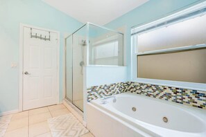 A bathroom with a glass shower enclosure, a white bathtub with a mosaic tile border, and a white door.