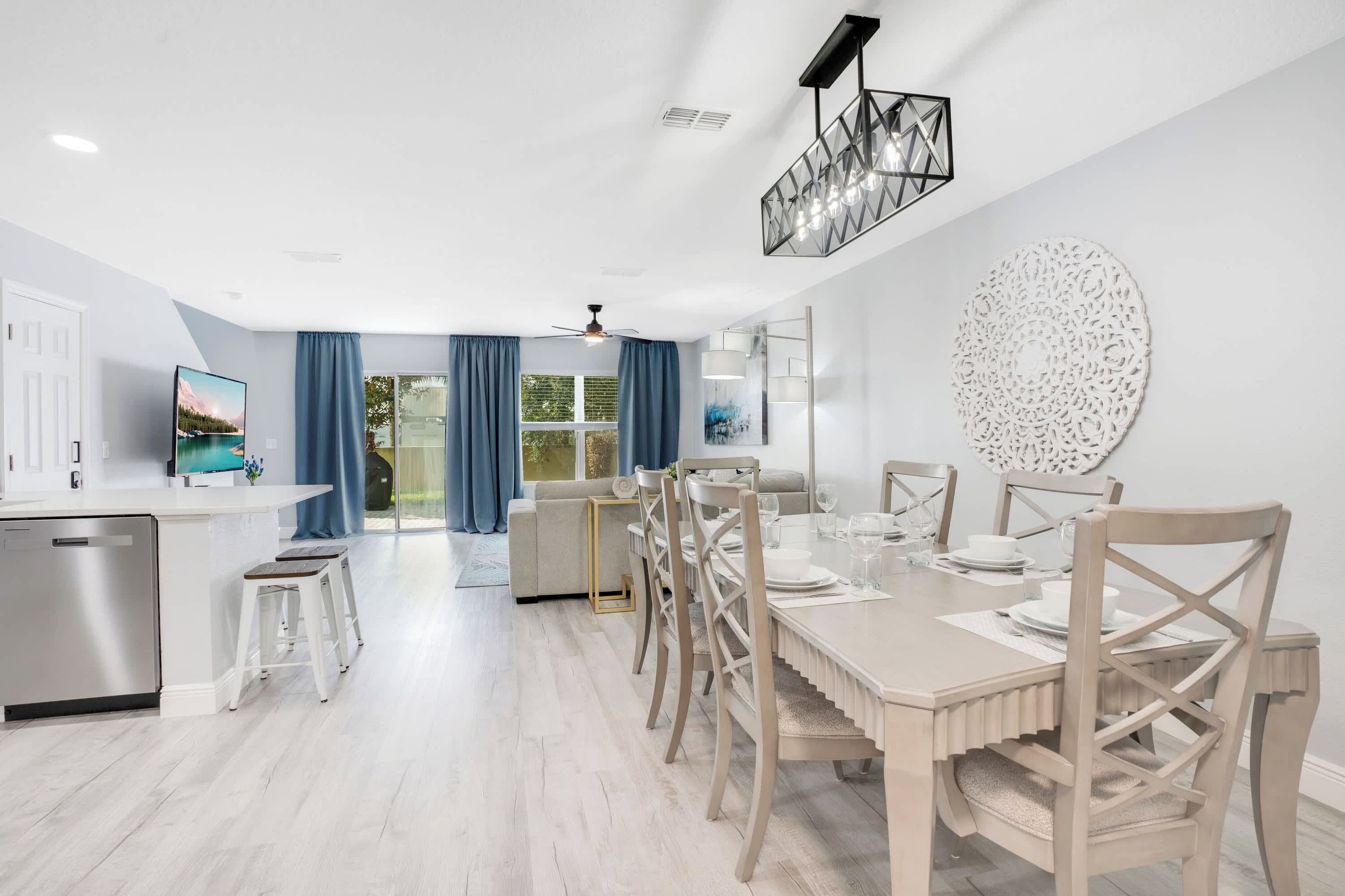 Eine moderne Küche mit integriertem Geschirrspüler, ein Essbereich mit einem langen Tisch und Stühlen sowie ein Wohnbereich mit Sofa und Fernseher.