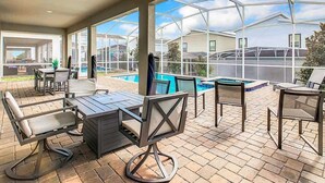 En udendørs patio med pool, overdækket siddeområde og udsigt til nabohuse.