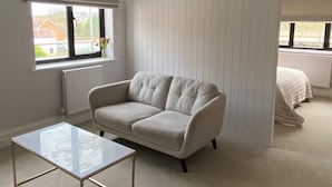 A modern bedroom with a large window, a beige sofa, a glass coffee table, and a white radiator. - Stunning 6-Bedroom House in Swanage, Minutes from Beach, with Parking and Garden (Swanage)