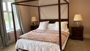 A four-poster bed with a white and beige bedspread, two bedside tables with lamps, and a window with curtains. - Stunning 6-Bedroom House in Swanage, Minutes from Beach, with Parking and Garden (Swanage)