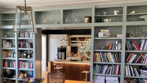 A dining area with a wooden table, chairs, and a vase of flowers. There are bookshelves on either side of the room filled with books and decorative items. - Stunning 6-Bedroom House in Swanage, Minutes from Beach, with Parking and Garden (Swanage)