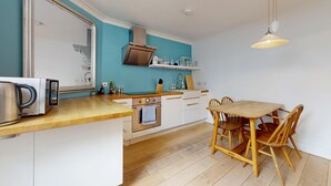 Una cucina moderna con mobili bianchi, un bollitore in acciaio inossidabile, un tavolo da pranzo in legno e un lampadario.