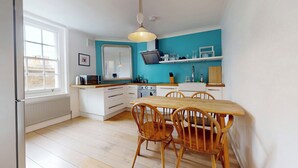 Una cucina con mobili bianchi, un tavolo da pranzo in legno e sedie, una finestra e un muro blu.