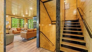 A wooden interior with a staircase, a living area with a sofa and a coffee table, and a large window. - Rustic Cabin Retreat・Sleeps 10・Indoor Pool・Hot Tub (Sevierville)